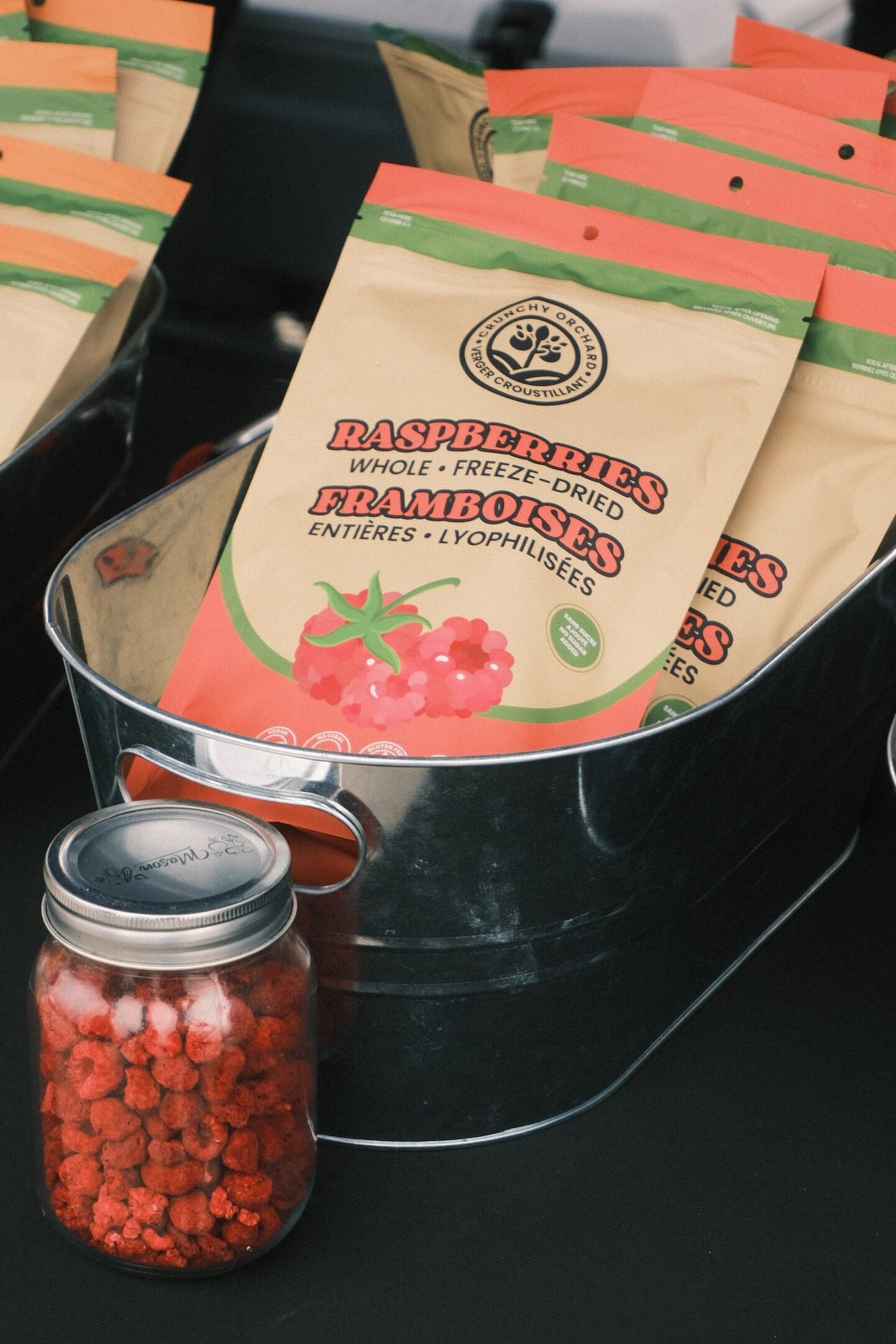 Framboises lyophilisées Verger Croustillant en sachets dans un bac et dans un pot en verre montrant la texture, au marché fermier