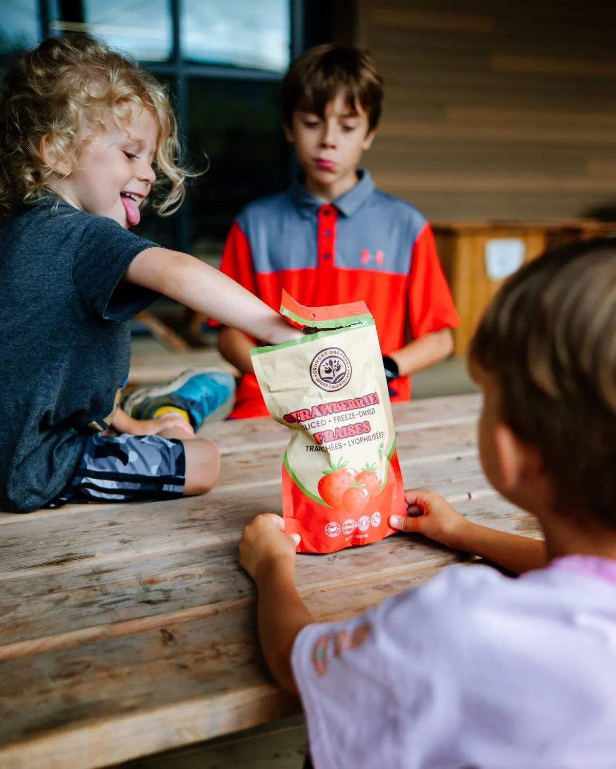 Kids at a table sharing a bag of Crunchy Orchard freeze-dried strawberries