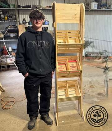 Hugo standing beside one of the wooden display racks he built for Crunchy Orchard